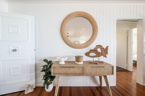 A room with a white door, a round mirror on the wall, a wooden console table with decorative items, and a potted plant. - A Point of View - Airlie Beach (Airlie Beach)