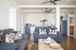 A modern living room with grey sofas, a wooden coffee table, and a kitchen in the background. - A Point of View - Airlie Beach (Airlie Beach)