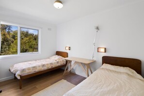 Ein Schlafzimmer mit zwei Einzelbetten, einem Schreibtisch und einem Fenster mit Blick auf Grünflächen.