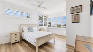 A bedroom with a wooden bed, white walls, and large windows with shutters.