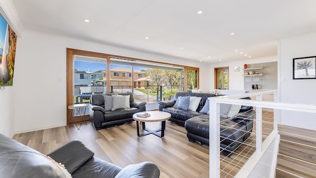 A modern living room with leather sofas, a coffee table, and large windows offering a view of the neighborhood.