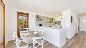 A modern kitchen with white cabinetry, a central island, and a dining area with white chairs and a wooden table.