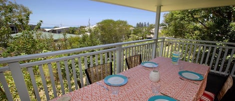 A covered outdoor dining area with a table set for four, surrounded by white railings and greenery.