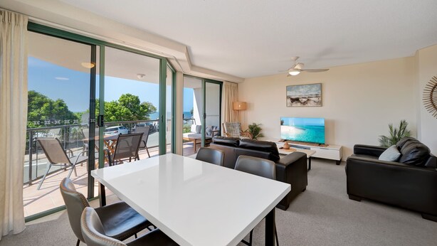 A modern living room with a balcony, a flat-screen TV, and a ceiling fan. - Seacrest Unit 2 Moffat Beach QLD (MOFFAT BEACH)