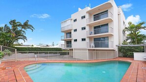 A modern multi-story building with balconies, a swimming pool, and palm trees. - Seacrest Unit 2 Moffat Beach QLD (MOFFAT BEACH)