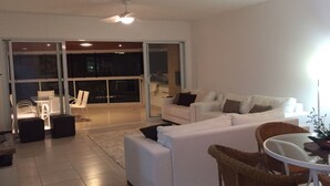 Ein modernes Wohnzimmer mit einem weißen Sofa, einem Esstisch, Korbstühlen und einer Glastür, die auf einen Balkon führt.