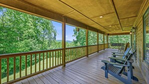 Una terraza techada con barandas de madera, una mesa y sillas, con vistas a un área boscosa.