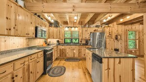 Una cocina de estilo cabaña de madera con encimeras de granito, un refrigerador de acero inoxidable y un ventanal grande.