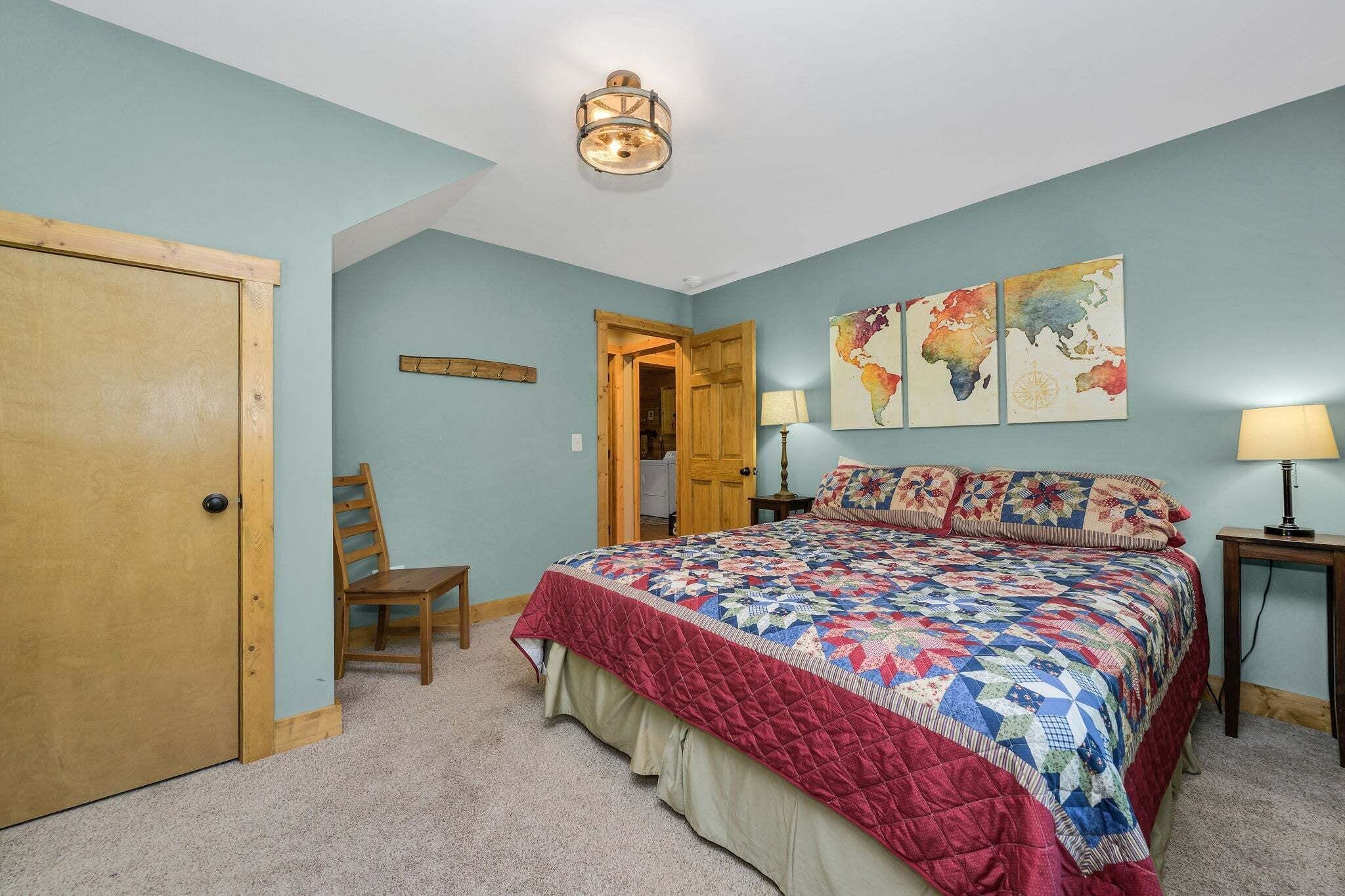 Ein Schlafzimmer mit einem Bett, einer Holztür, einem Stuhl, einer Karte an der Wand und einer Deckenleuchte.