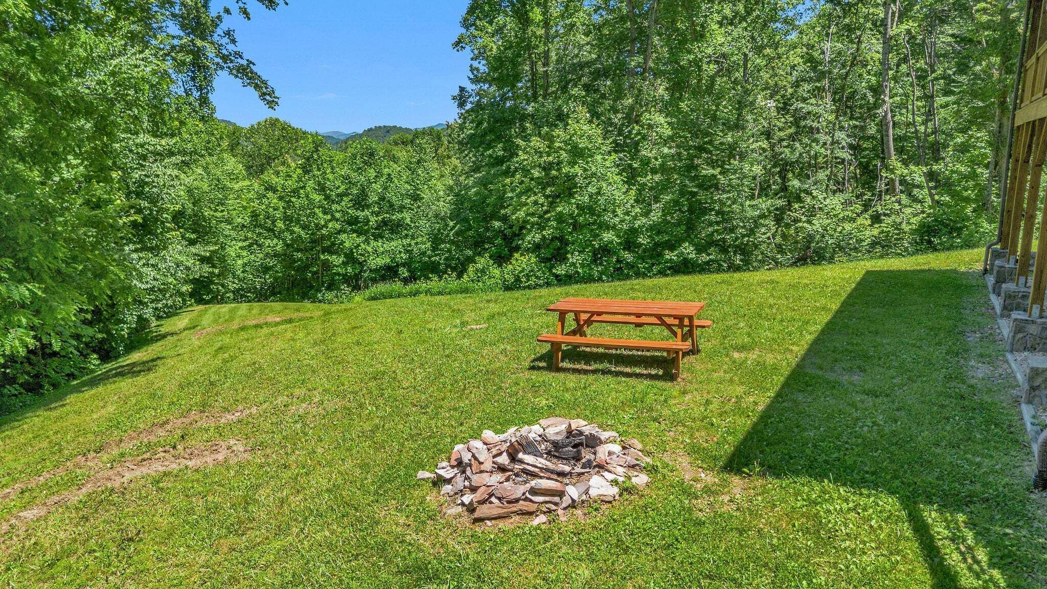 A picnic area with a wooden table and a fire pit surrounded by grass and trees.