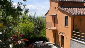 A building with a tiled roof, a balcony, and a gravel driveway leading to a white table and chairs set. - Friendly Quiet Rustic 6/8 Sleeps Apt Near Woods (Pisa)