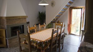 A dining area with a brick fireplace, wooden chairs, a table with a floral tablecloth, a hanging light fixture, and a staircase leading to a balcony. - Friendly Quiet Rustic 6/8 Sleeps Apt Near Woods (Pisa)