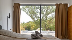 A bedroom with a large window, a bed, and a view of an outdoor area with a pool and lounge chairs. - Luxury Modern Seaview Villa  With  Private Pool In Klimno ***** (Klimno)