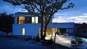 A modern two-story house with a swimming pool, outdoor seating, and a large tree in the foreground. - Luxury Modern Seaview Villa  With  Private Pool In Klimno ***** (Klimno)