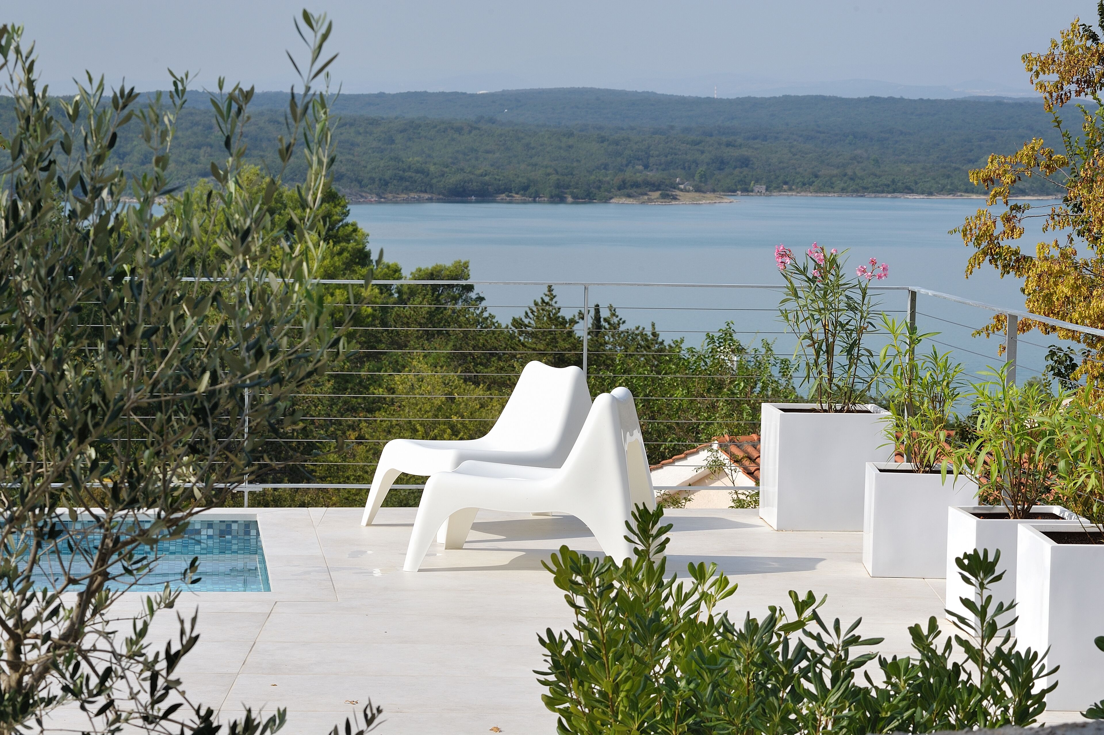 A modern outdoor seating area with a pool, overlooking a lake and hills.