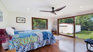 Ein Schlafzimmer mit einem großen Bett, einem Deckenventilator und einer Schiebetür, die zu einem Garten führt.