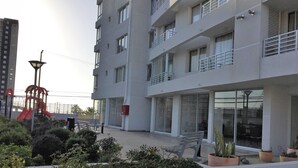 Un edificio moderno con varios balcones, un parque infantil y plantas en macetas.