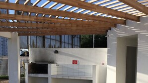Un espacio de patio exterior con pérgola, una parrilla empotrada y una pared de azulejos blancos.