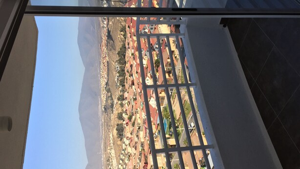 Vista a través de una ventana con barrotes, mostrando una zona residencial con casas y una montaña al fondo.