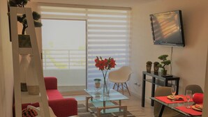 Una sala de estar moderna con una mesa de centro de vidrio, un sofá rojo y una zona de comedor con una mesa y sillas de vidrio.