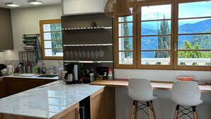A modern kitchen with a large island, wooden cabinets, and a view of the outdoors through large windows.