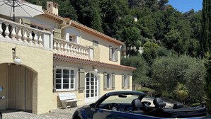A blue convertible car parked in front of a building with a tiled patio and a bench.