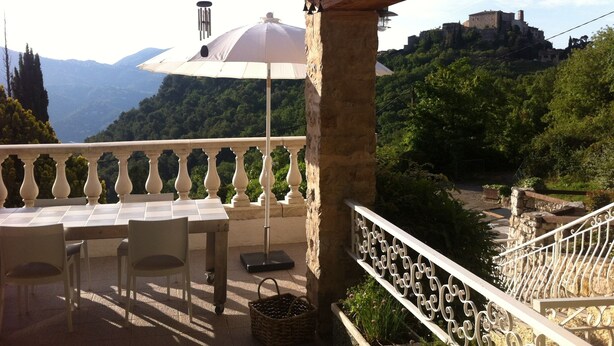 A terrace with a table and chairs, overlooking a mountainous landscape with a castle.