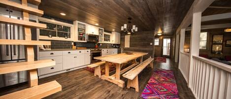 A modern kitchen with wooden beams, white cabinets, and a large wooden table.