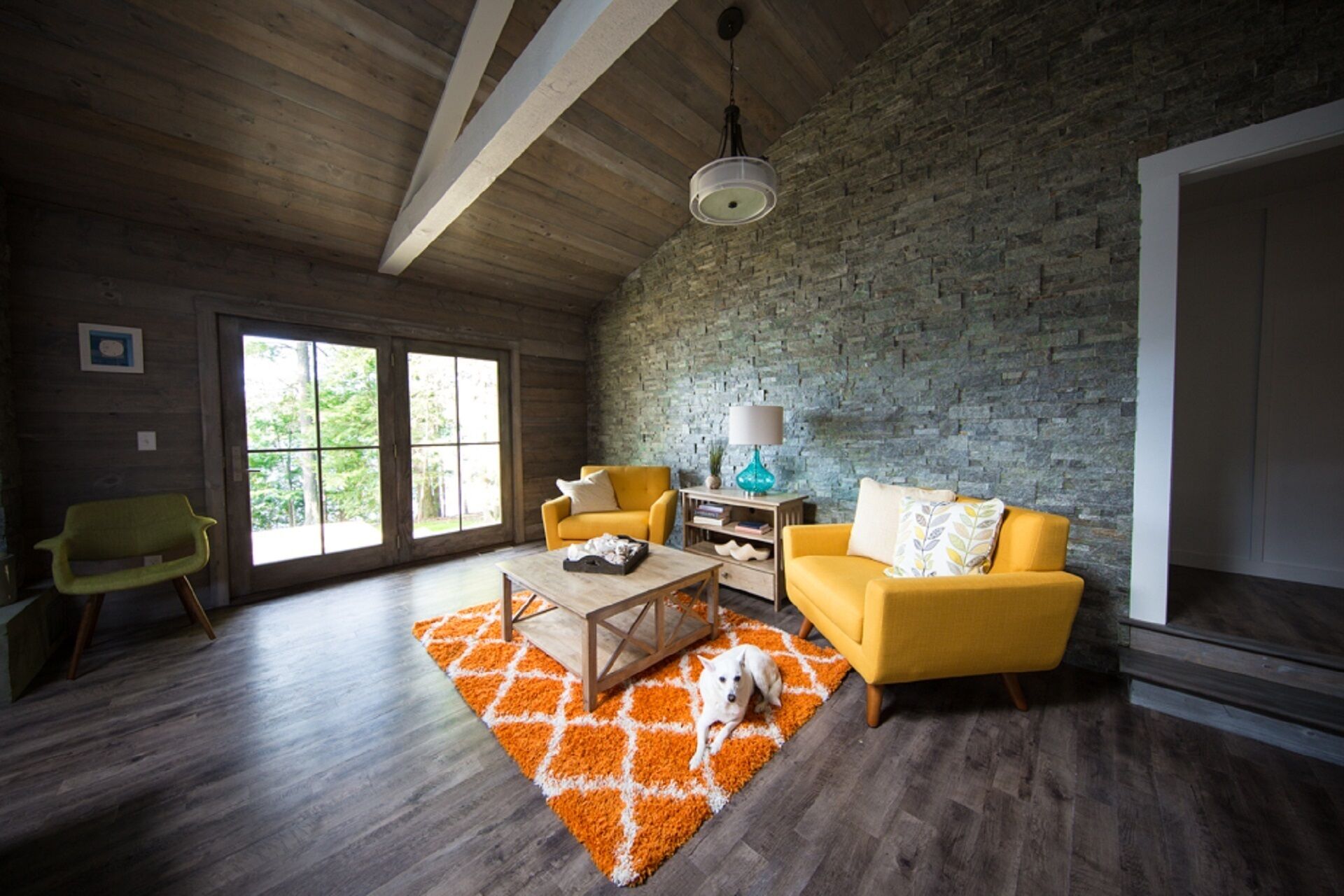 Un salon spacieux avec un plafond haut, des poutres en bois, un mur en pierre et une grande fenêtre.