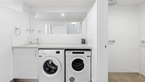 A modern laundry room with two front-loading washing machines, a sink, and a mirror above.