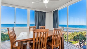 Comedor con vistas al mar, que incluye una mesa y sillas de madera, ventanas grandes y un ventilador de techo.