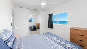 Un dormitorio con cama, cómoda, ventana con vista al mar y ventilador de techo.