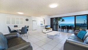 A modern living room with a dining area, a TV, and a balcony with a view of the sea.