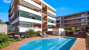A multi-story hotel with a swimming pool, outdoor seating, and a fenced garden area.