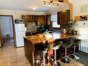 A kitchen with wooden cabinets, a central island with stools, a refrigerator, and a microwave.