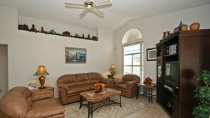 A living room with a brown leather sofa set, a coffee table, a TV stand, and a ceiling fan. - Waterview ,Private Pool, Family Friendly, Spacious and Relaxing (Kissimmee)