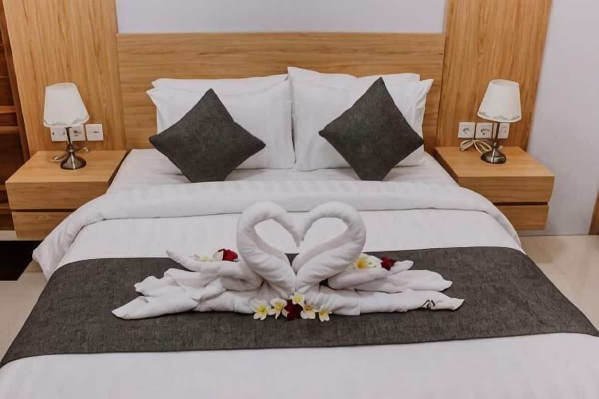 Habitación de hotel con cama, dos mesitas de noche, una decoración de toallas con forma de corazón y una manta gris.