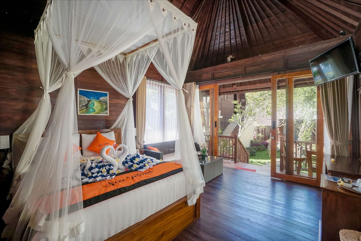 A bedroom with a canopy bed, a television, and a view of the outdoor area.