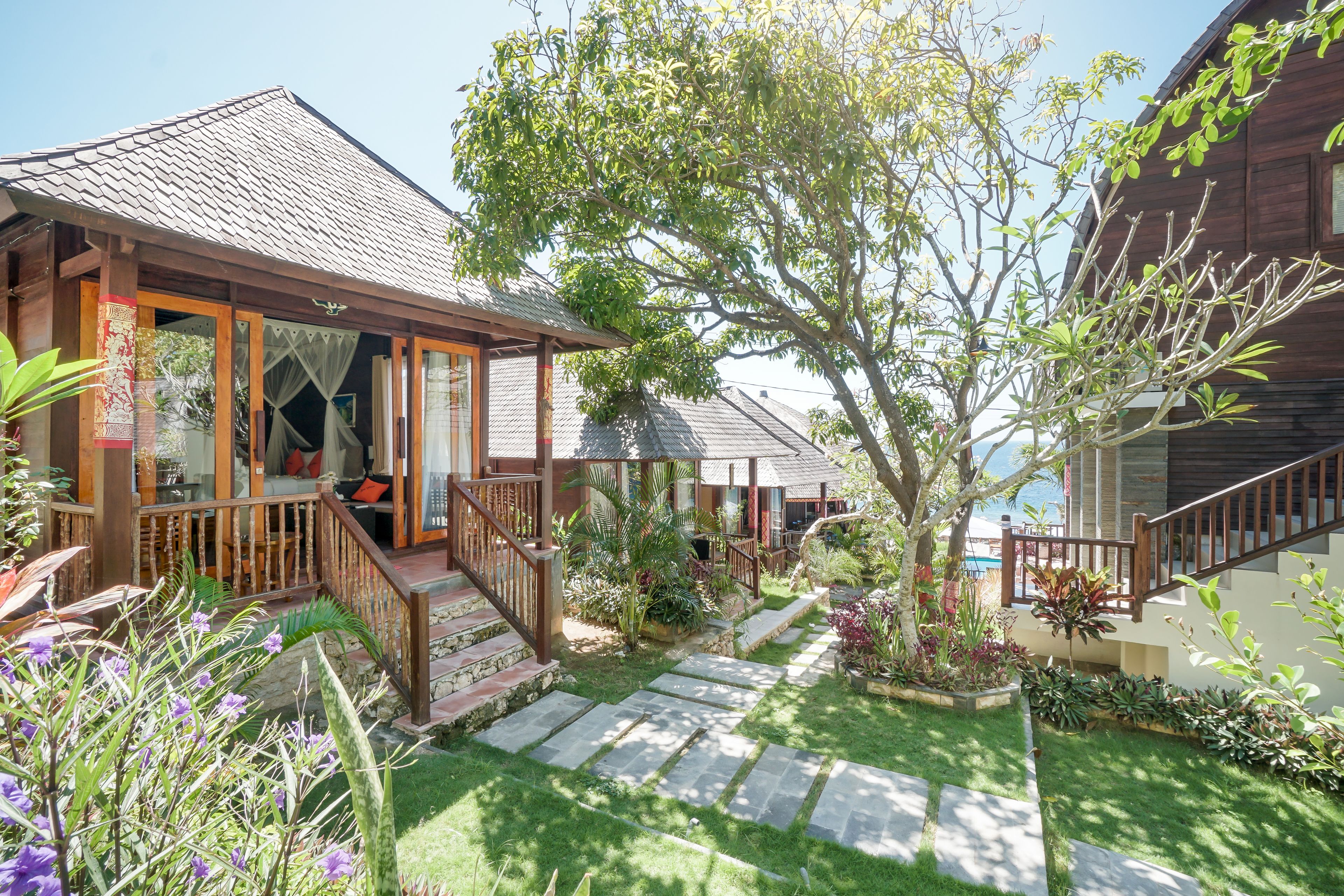 A wooden house with a tiled roof, a porch with a wooden railing, and a stone pathway leading to the entrance.