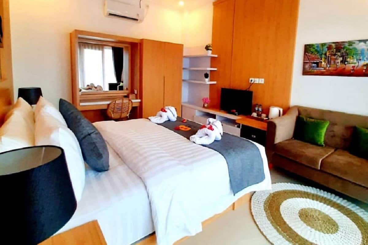 A hotel room with a bed, a desk, a TV, a sofa, and a painting on the wall.