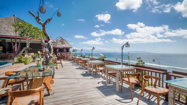 Une terrasse extérieure avec des meubles en bois et une table en verre, offrant une vue sur l’océan.