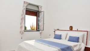 Een slaapkamer met een bed, een raam met bloemen gordijnen en uitzicht op bomen.