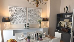 A dining area with a white table set for four, surrounded by white chairs. There are decorative wall panels above the table, a chandelier, and a bookshelf with framed pictures and books. - Fabulous 200sqm bright, new apartment walking distance to Duomo and city centre (Firenze)