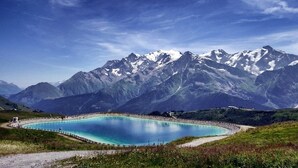 A mountain landscape with a large turquoise lake surrounded by rocky terrain and snow-capped peaks. - Appartement Cosy 3 pièces | Ski, Sauna (Saint Gervais)