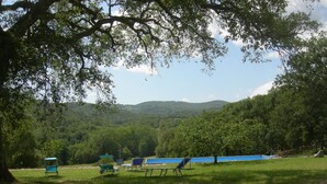 A park with picnic tables, a blue swimming pool, and a view of a forested hillside.