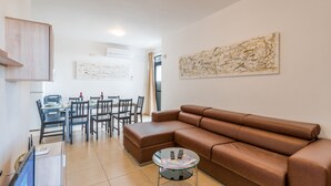 A modern living room with a brown leather sofa, a glass coffee table, and a dining area with a table and chairs. - Bugibba - 2 bedroom apt 150m from Sea Front Fully Air Conditioned, Terraces WiFi (Bugibba,)