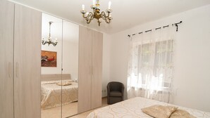 Ein Schlafzimmer mit Bett, einem Sessel, einem Kleiderschrank, einer Deckenleuchte und einem Fenster mit Vorhängen.