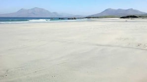 A wide sandy beach with calm water and distant mountains.