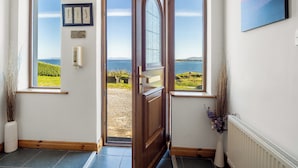 A room with a view of the sea through two windows, a door leading outside, and a framed certificate on the wall.