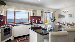 A modern kitchen with white cabinets, a large window overlooking a body of water, and a dining area with a table and chairs.